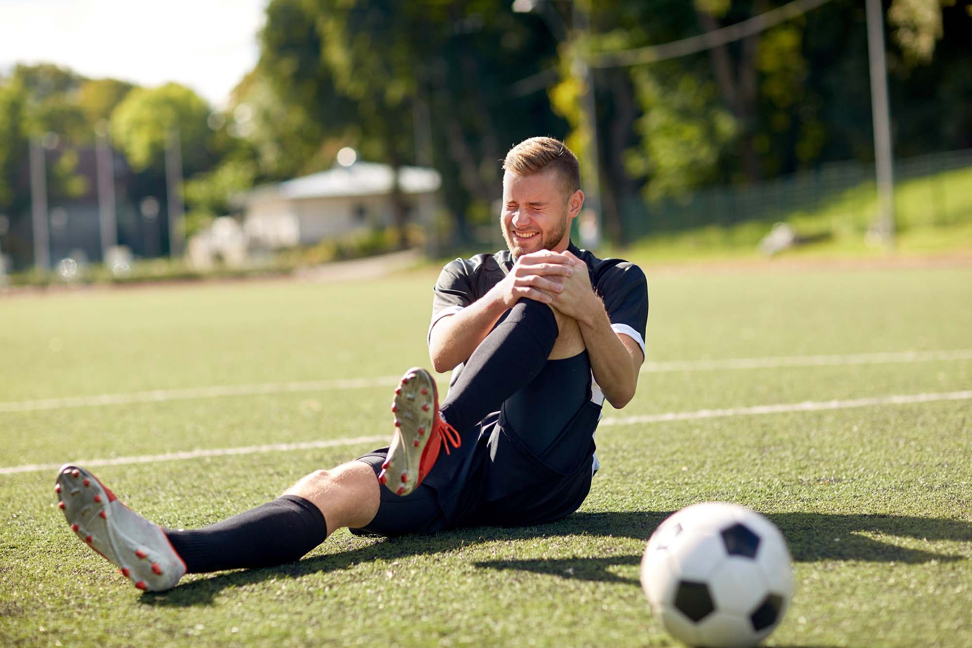 Sport, football training, sports injury and people - injured soccer player with ball on field