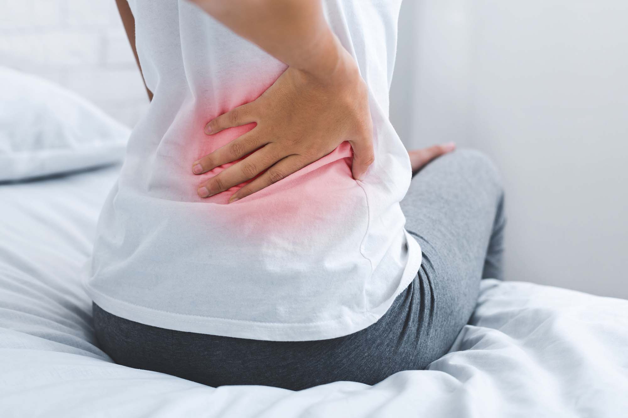 Woman suffering from back pain, having spinal or lower back problem, sitting on bed