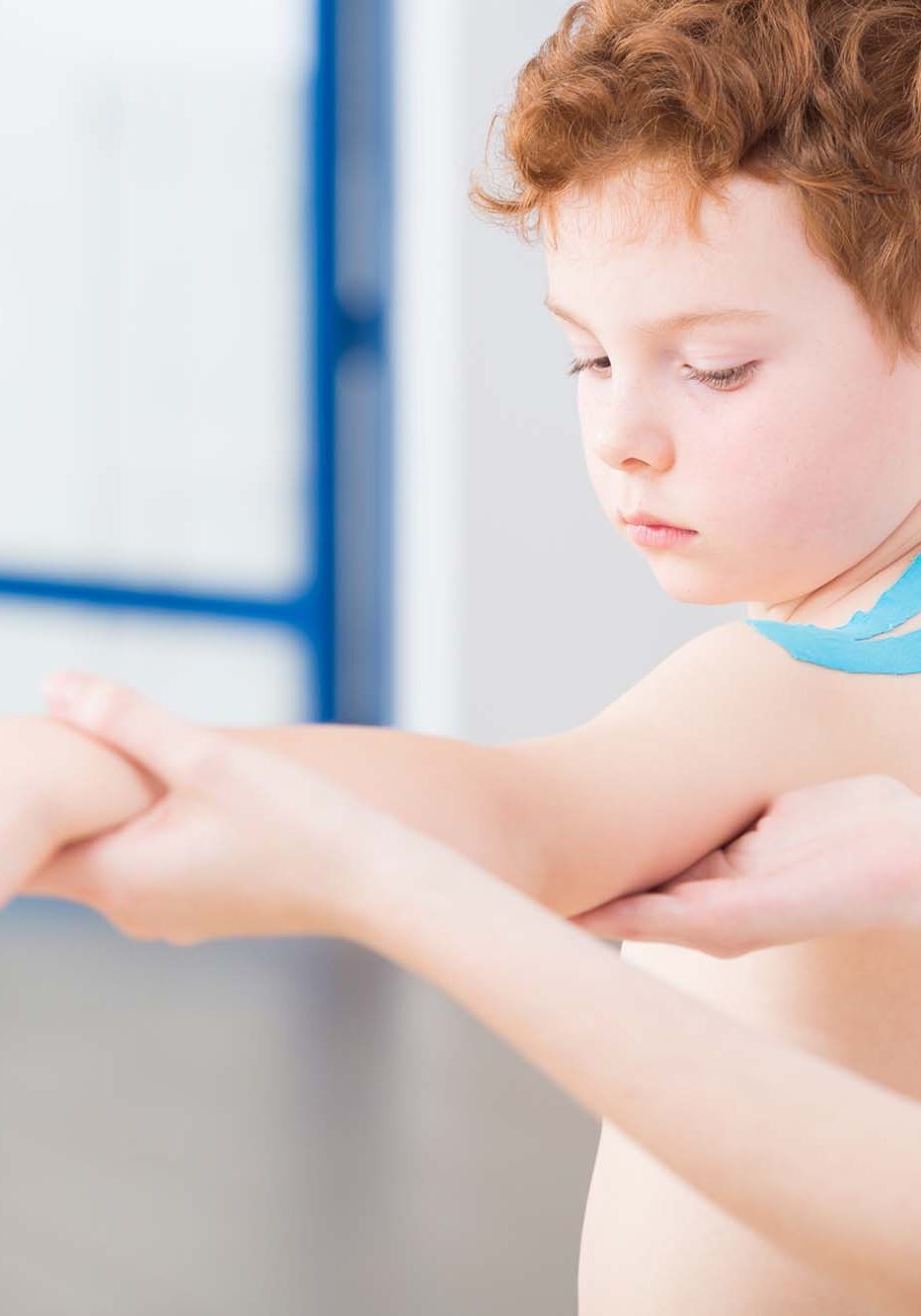 Little cute red head boy having arm problem after injury. Physical therapist treating the patient with exercises